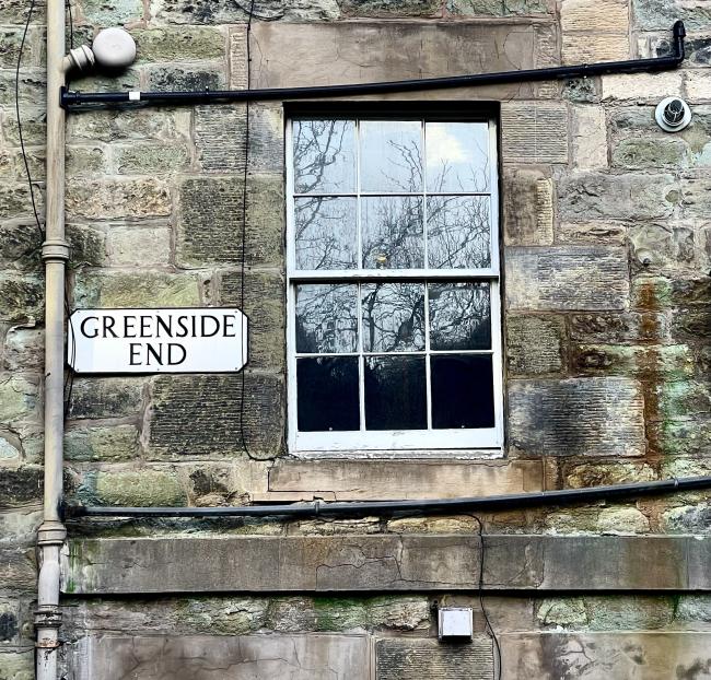 Sign on wall with patches of green algae on masonry.