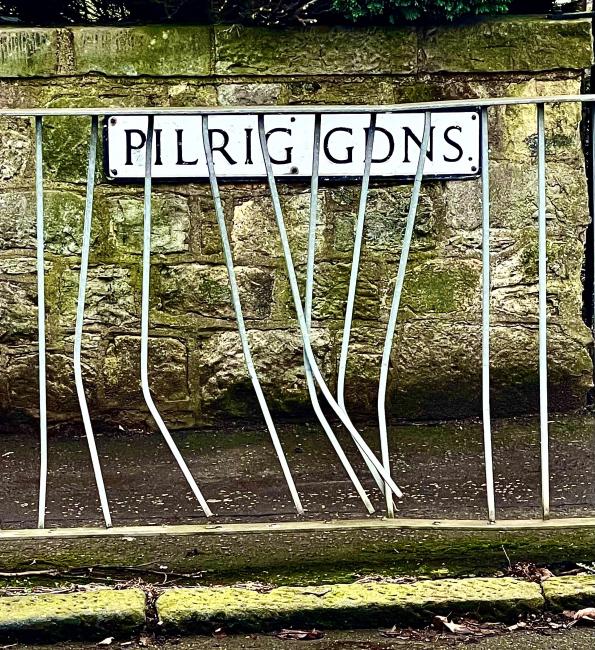 Street-name sign behind railings bent like dancers' legs.