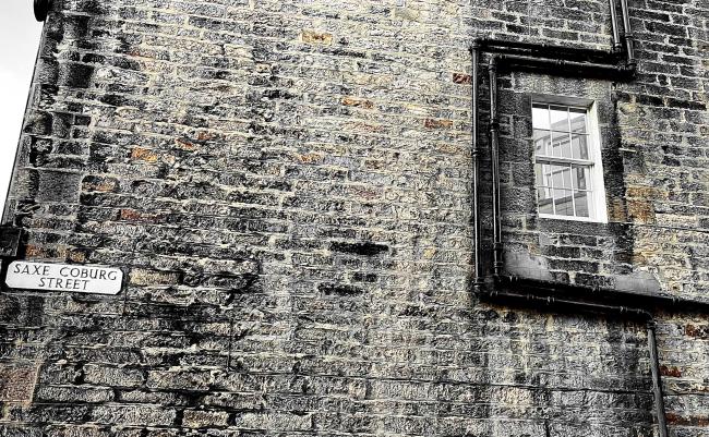 Gable-end masonry and downpipes circumventing a sash window.